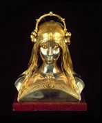 A bust of a young woman with eyes cast downward, an ornamental neckline  and a tall, arched crown with silver lilies on the sides
