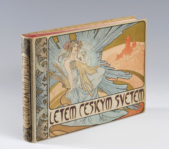 A landscape format book seen from the side on with a woman surrounded by blue stylised feathers with poppies in her hair and a red Bohemian style castle on a rock behind; decorative vertical border on the left side; title in the lower third of the cover
