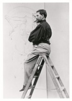 Mucha sitting on the left side of a stepladder in front of a large pencil drawing smoking a cigar and looking out to the left