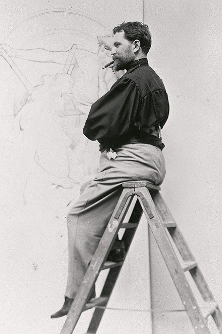 Mucha sitting on the left side of a stepladder in front of a large pencil drawing smoking a cigar and looking out to the left
