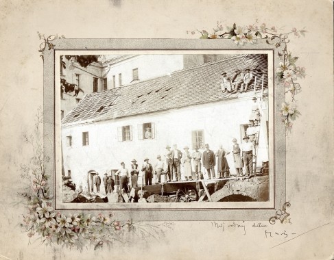 Mucha's birthplace A photo od a line or men standing in a line in front of a long white building with two men standing on a ladder and three men sitting on the roof; the photo has a hand-drawn border with flowers and a hand-written inscription on the bottom right