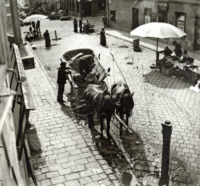 A street scene seen from above with horses and a cart and market sellers under parasols