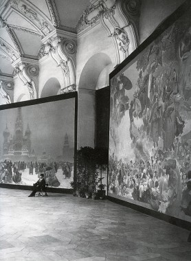 Slav Epic canvases A man sits on a stool in front of two of the Slav Epic canvases
