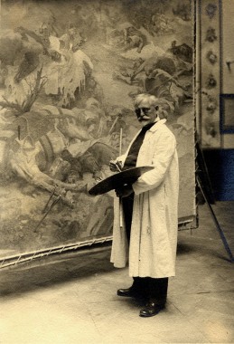 Mucha working on the Slav Epic Mucha standing in overalls with a palette in front of one of his Slav Epic canvases