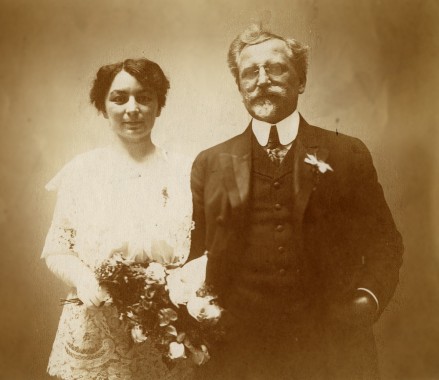 Wedding photo of Alphonse and Maruška Mucha The couple in formal clothes against a dark background; Maruska holds a bouquet in her right hand and links arms with her husband