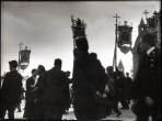 Taken about a foot from ground level, a procession of men in black holding religious effigies march against an ominous grey sky