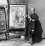 Moulin Rouge – La Goulue Two men standing next to a poster with a woman at centre stage performing the can-can to an audience of men in top hats, with the words 'Moulin Rouge - La Goulue - Tous les soirs'