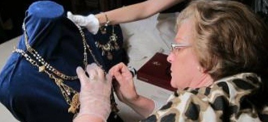 Conservator working on a piece of jewellery assisted by a lady who holds the piece of jewellery in place