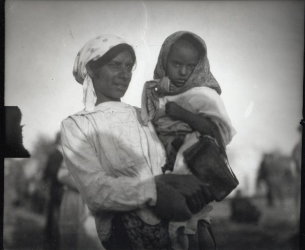 A dark-haired women with a white polka dot headdress holding a small child with a headdress